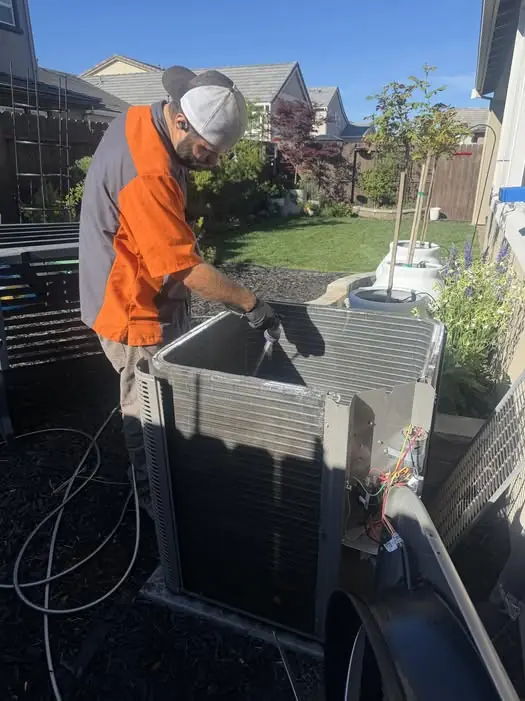 AccuFlow technician cleaning the coil of an outdoor AC condenser during service