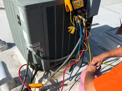 AccuFlow technician checking refrigerant pressures on a rooftop AC condenser with gauges